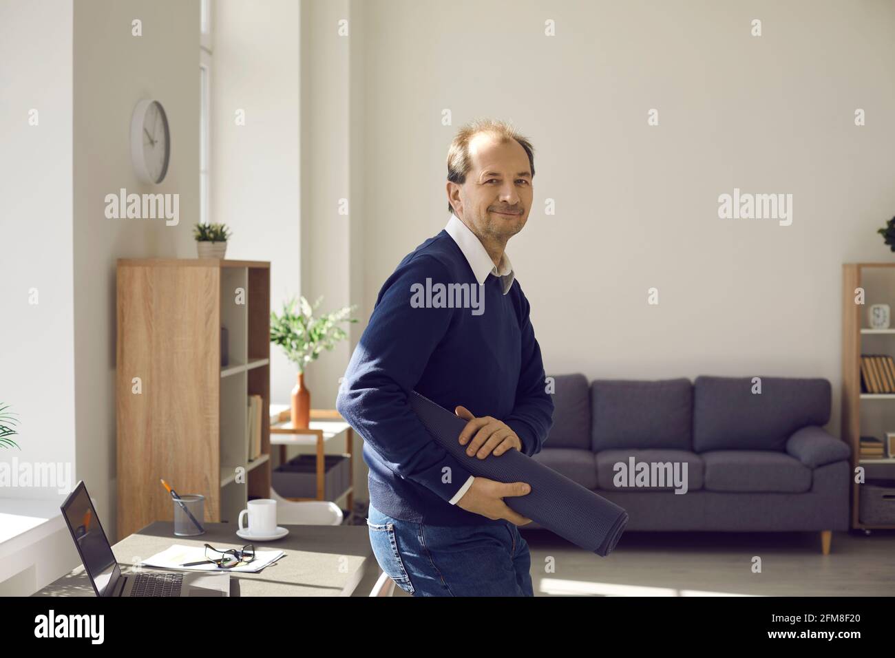Ritratto di un uomo adulto sorridente che cammina con lo yoga tappetino per l'esercizio Foto Stock