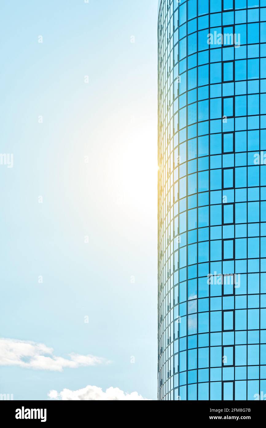 Alto ed elegante edificio per uffici con una facciata di vetro blu brillante che si riflette luce solare chiara contro il cielo blu chiaro nella giornata di sole Foto Stock