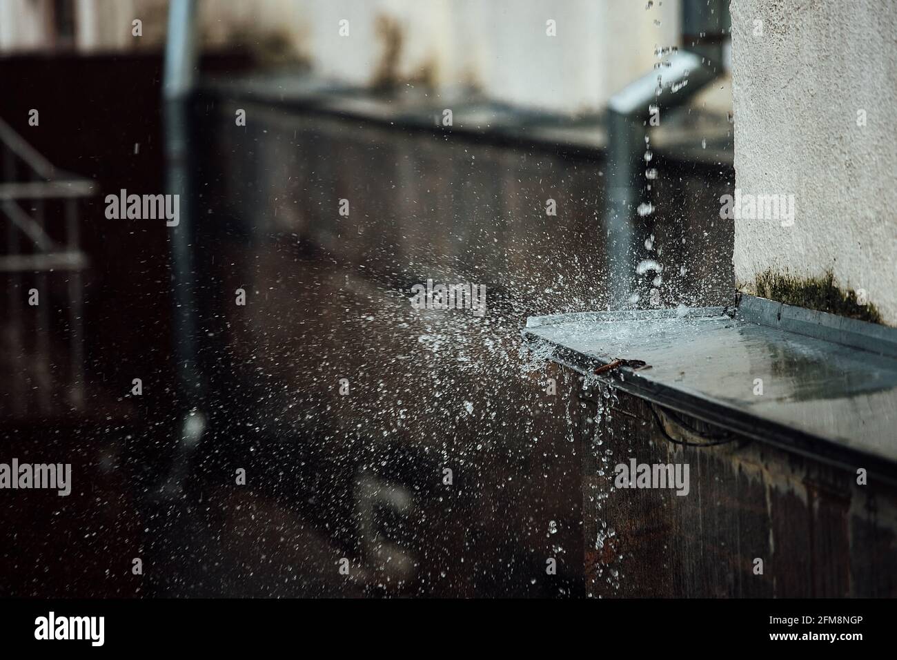 gocce di pioggia cadenti si rompono sulla sporgenza. spruzzi da acqua corrente. tubo di scarico dal tetto di un edificio durante una tempesta di pioggia Foto Stock