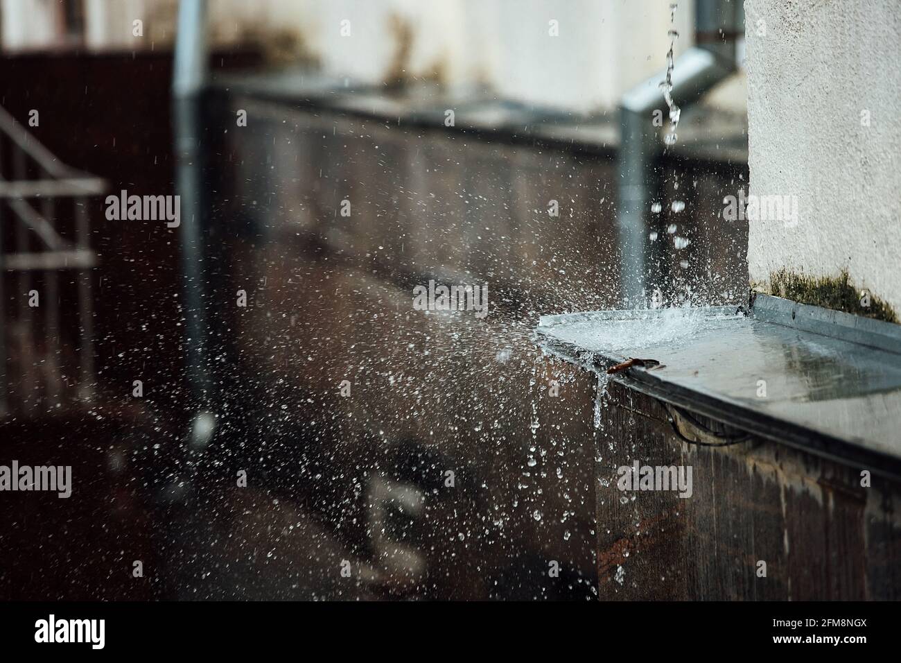 gocce di pioggia cadenti si rompono sulla sporgenza. spruzzi da acqua corrente. tubo di scarico dal tetto di un edificio durante una tempesta di pioggia Foto Stock