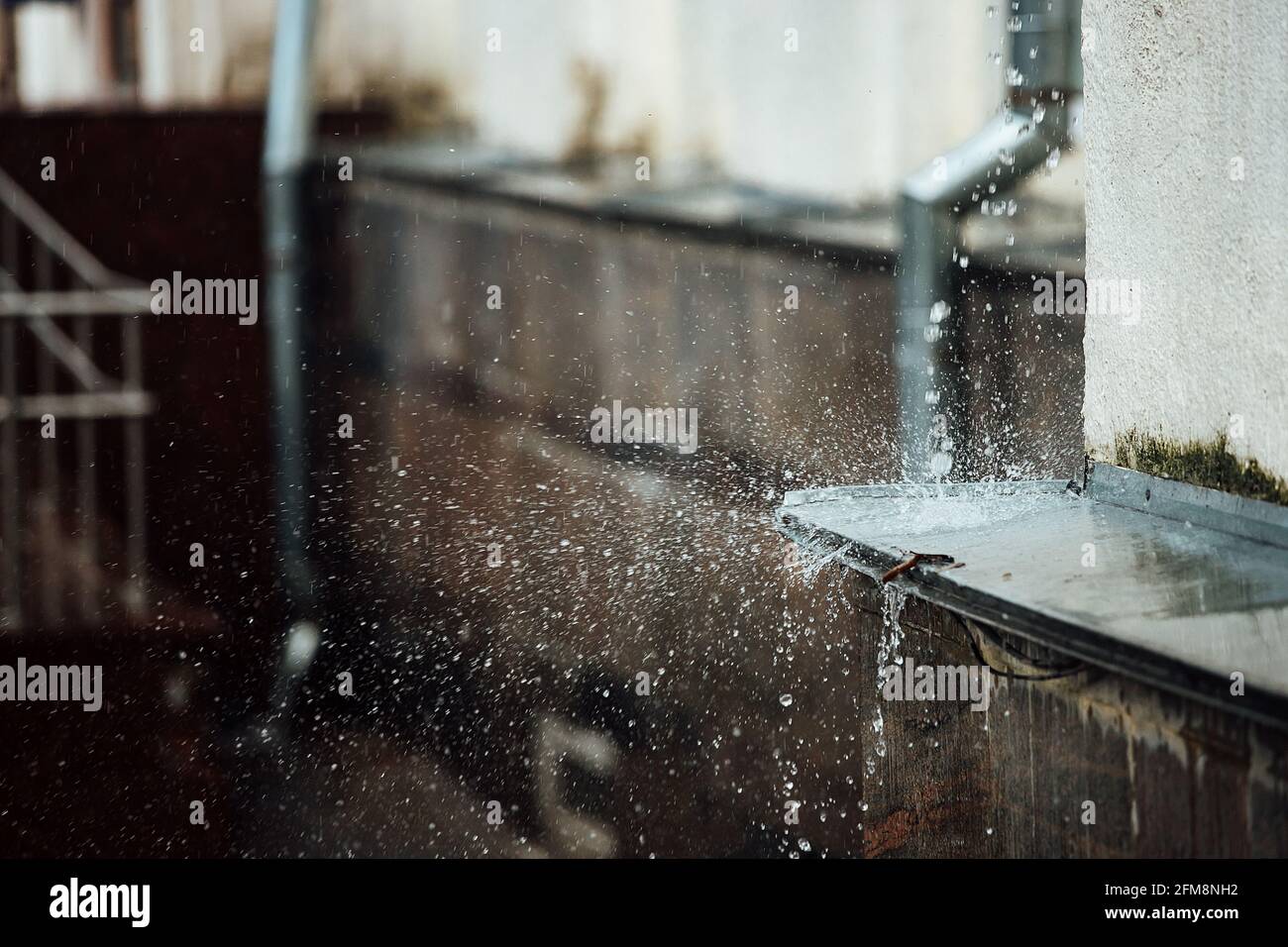 gocce di pioggia cadenti si rompono sulla sporgenza. spruzzi da acqua corrente. tubo di scarico dal tetto di un edificio durante una tempesta di pioggia Foto Stock