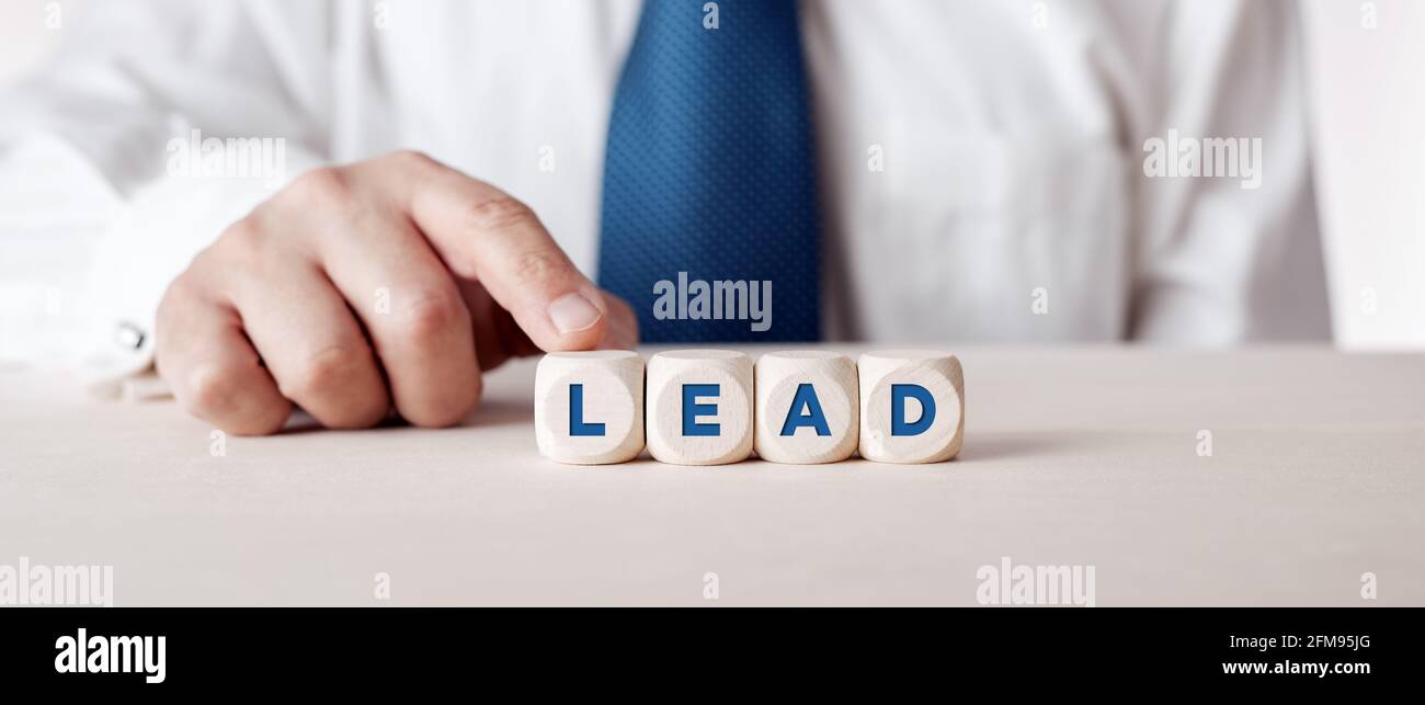 Uomo d'affari premendo il dito sui cubetti di legno con la parola piombo. Concetto di leadership organizzativa o di mercato. Foto Stock
