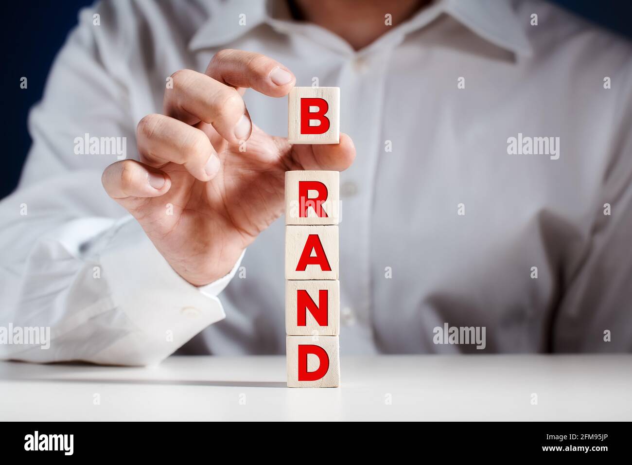 Uomo d'affari mette un cubo sulla cima di cubetti di legno a più livelli con la parola marca. Concetto di business di brand building. Foto Stock