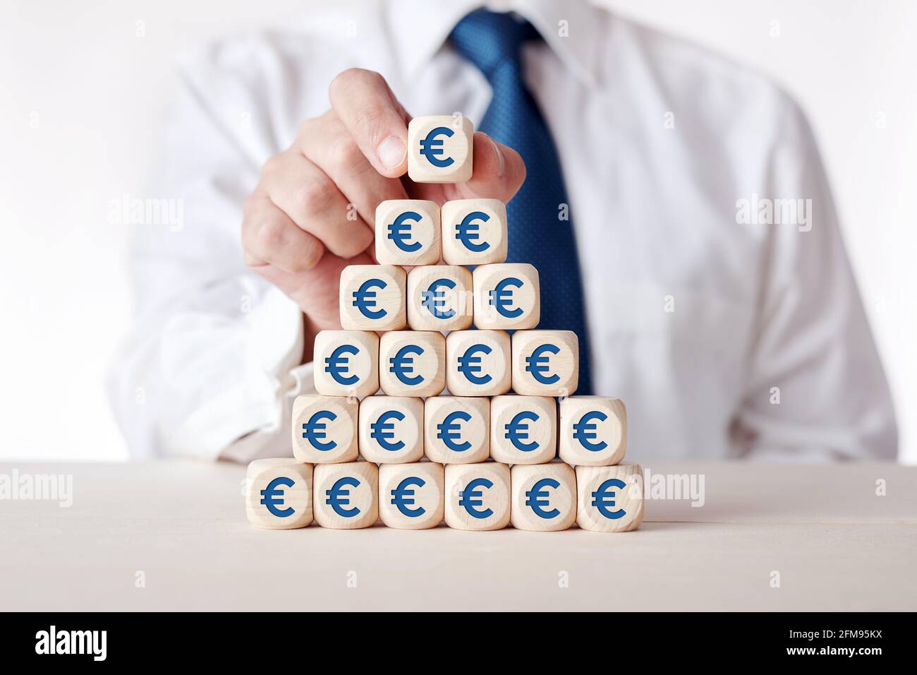 Investimento finanziario, risparmio, tasse o aumento dei profitti concetto. L'uomo d'affari mette i cubetti di legno a più livelli con il simbolo del denaro dell'euro. Foto Stock