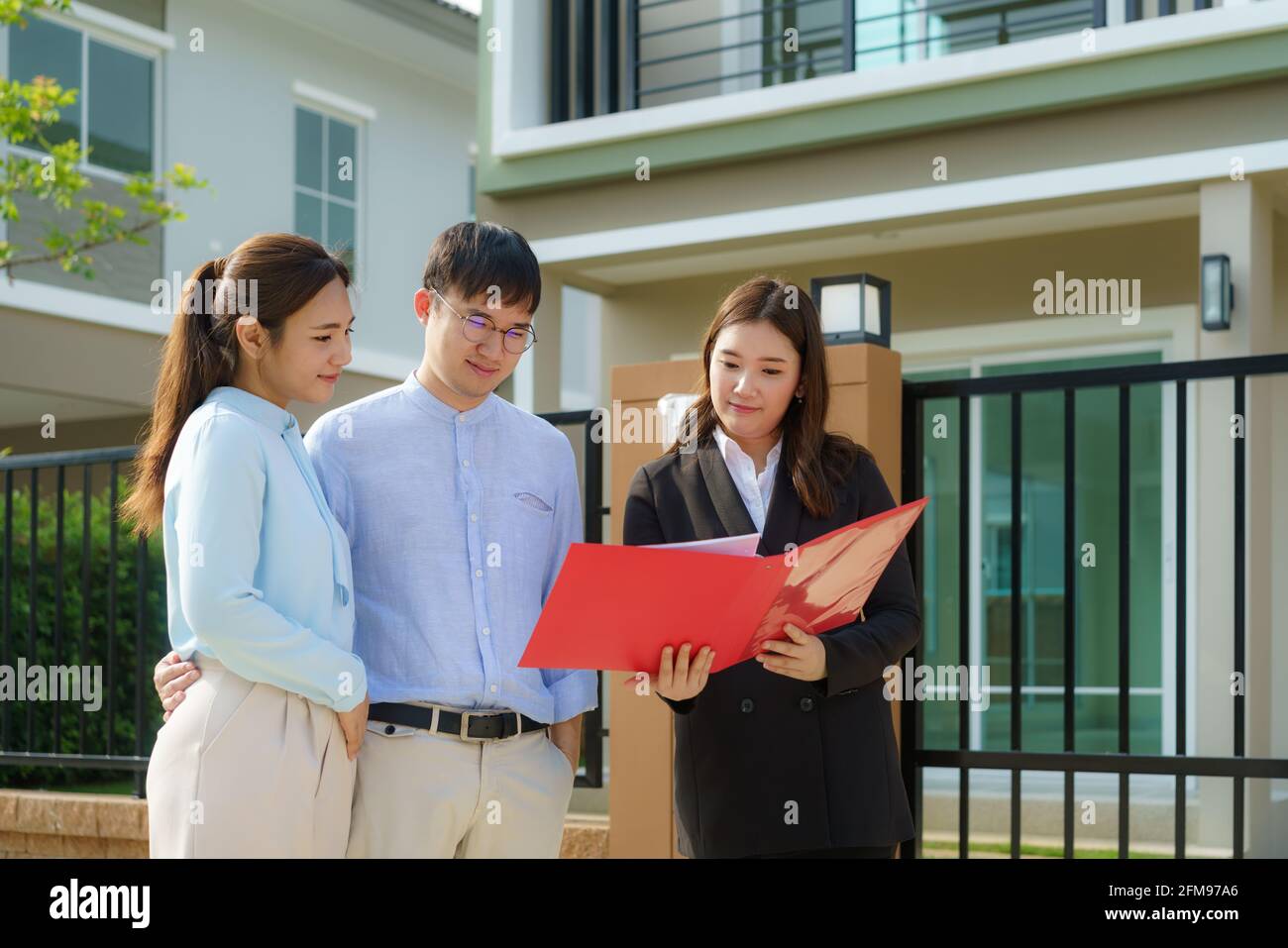 Donna asiatica Agente broker immobiliare che mostra un dettaglio della casa nel suo file per la giovane coppia asiatica amante cercando e interesse a comprarlo. Acquisto di una nuova ora Foto Stock