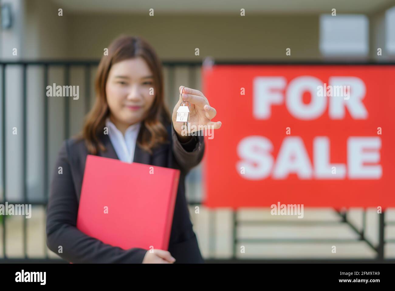 Agente immobiliare asiatico o donna immobiliare sorridente e tenendo file rosso con mostrare la chiave di casa di fronte alla casa. Foto Stock