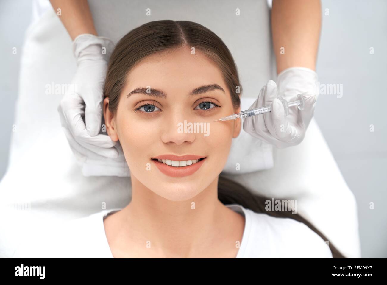 Vista dall'alto ritratto di sorridente bella giovane donna bruna sulla procedura per miglioramenti della pelle. Concetto di processo stringere la pelle dalle rughe in estetista professionista. Foto Stock