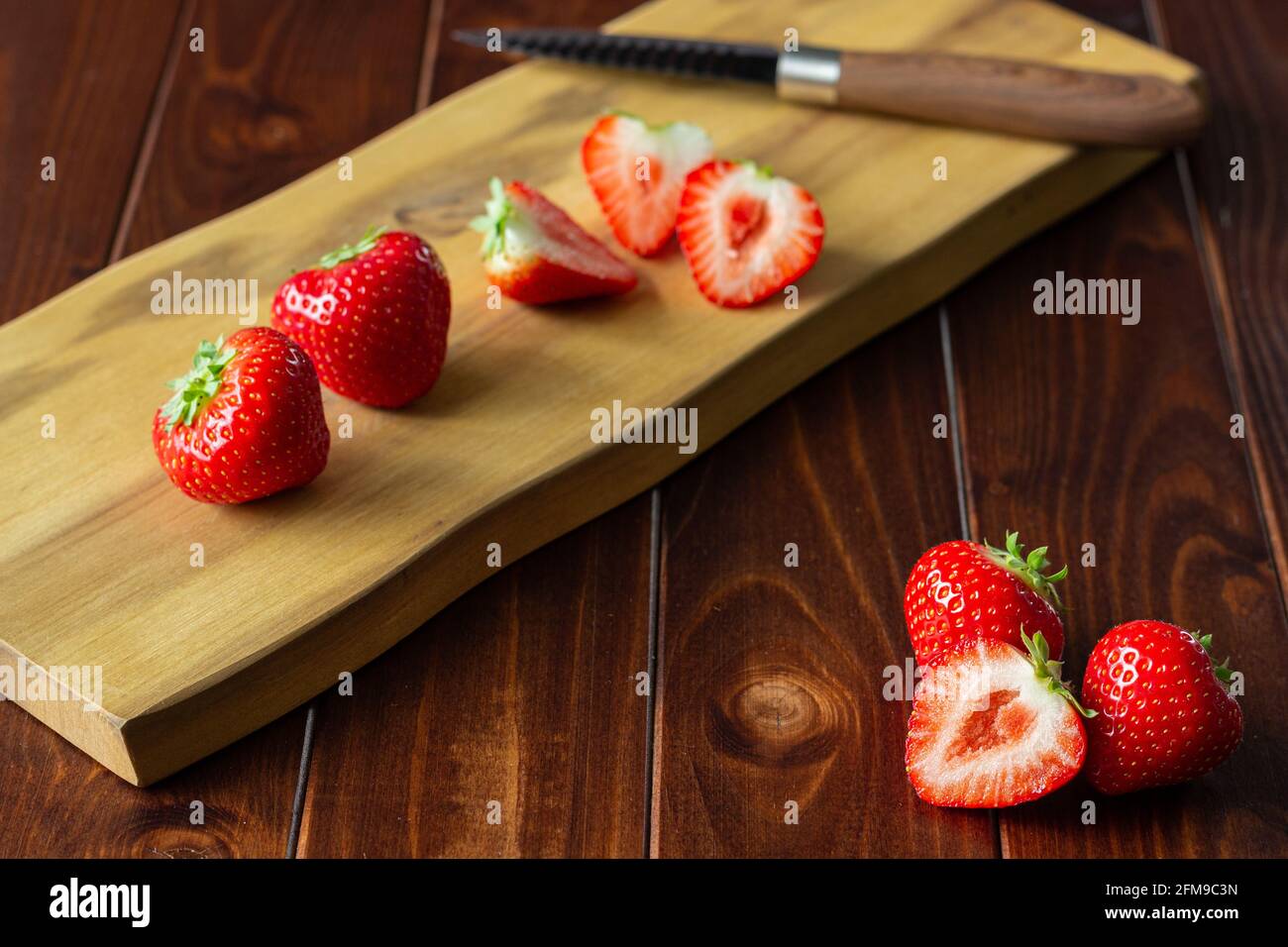 Primo piano di fragole perfettamente rosse su tavola da taglio in legno legno scuro Foto Stock
