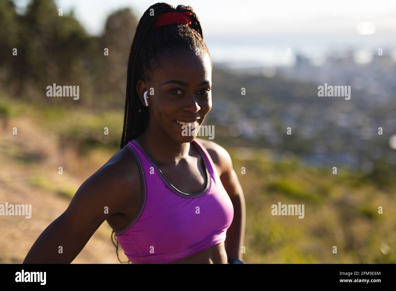 Ritratto di donna afroamericana in forma sorridente con auricolari wireless, che si esercita in campagna Foto Stock