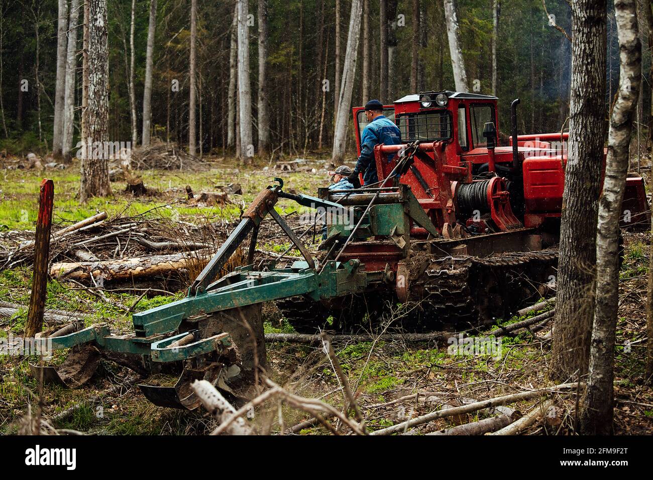 un trattore cingolato sta guidando attraverso uno sgombero forestale. un bulldozer industriale è bloccato nel fango. i camion stanno scivolando nel terreno Foto Stock