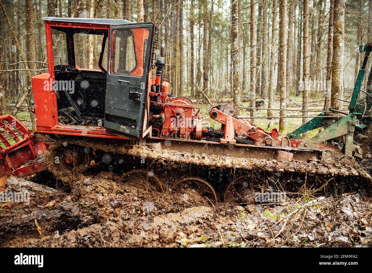 un trattore cingolato sta guidando attraverso uno sgombero forestale. un bulldozer industriale è bloccato nel fango. i camion stanno scivolando nel terreno Foto Stock