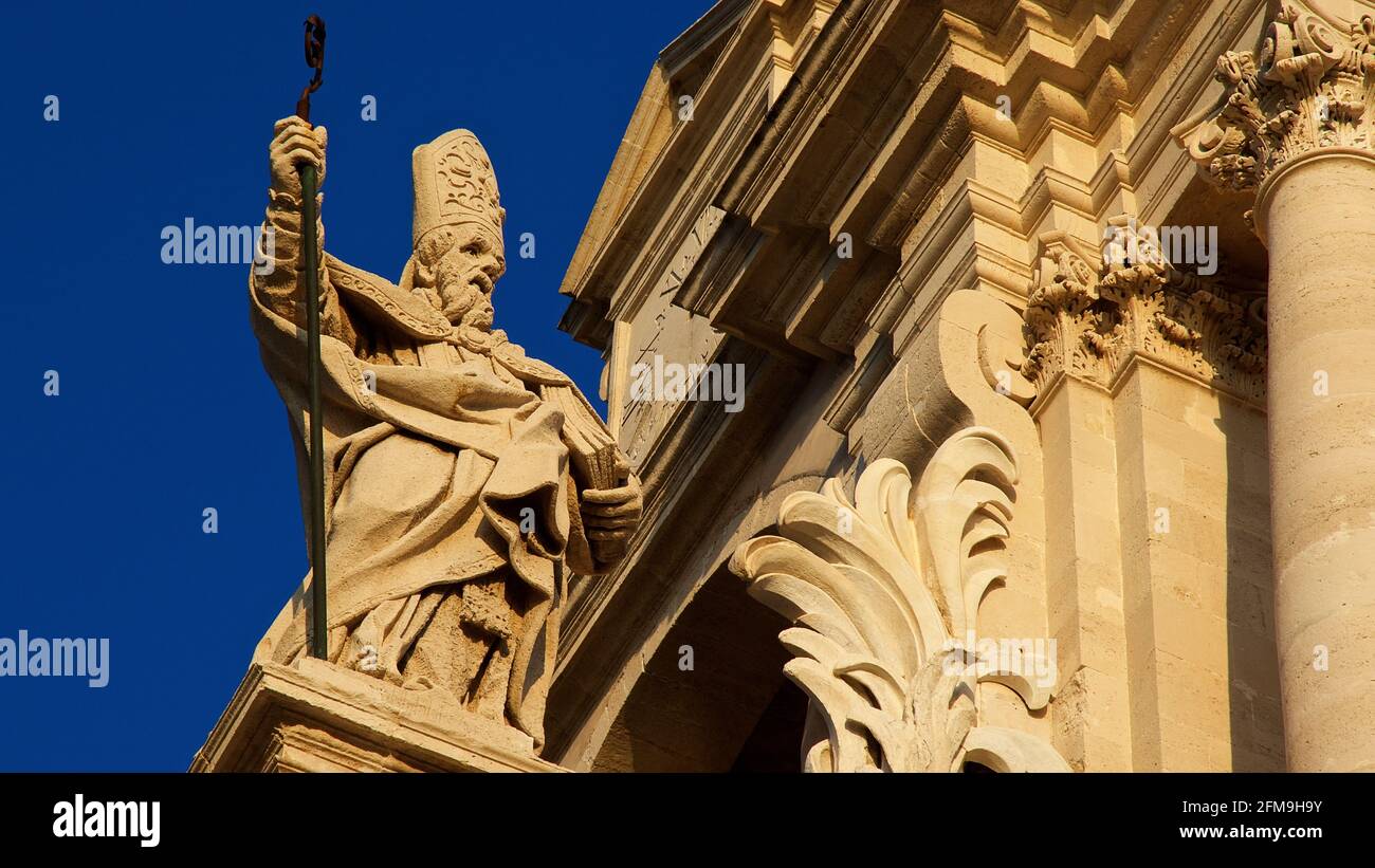 Italia, Sicilia, Siracusa, Penisola di Ortigia, Isola di Ortigia, Cattedrale di Siracusa, luce serale, figura santa sul tetto con il crook del pastore, cielo blu Foto Stock