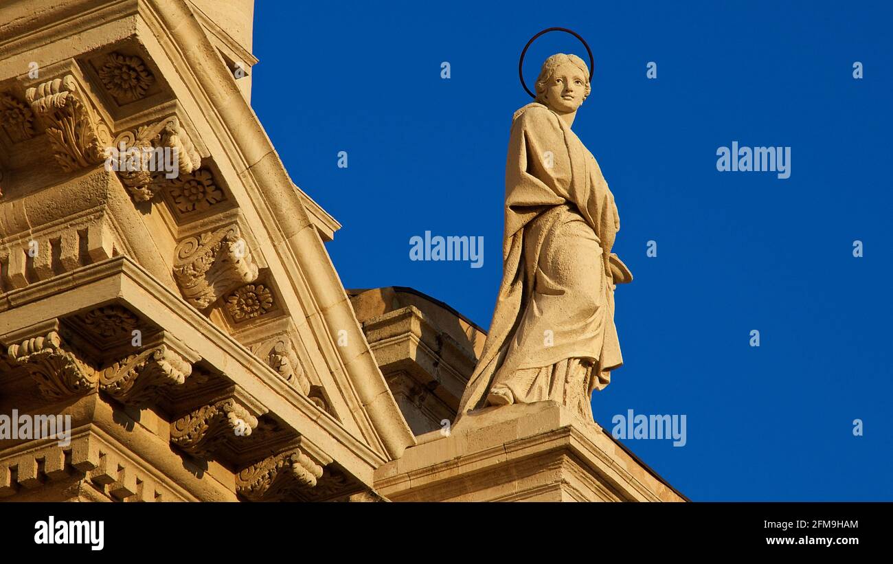 Italia, Sicilia, Siracusa, Penisola di Ortigia, Isola di Ortigia, Cattedrale di Siracusa, luce serale, santa figura sulla sporgenza del tetto, cielo blu Foto Stock