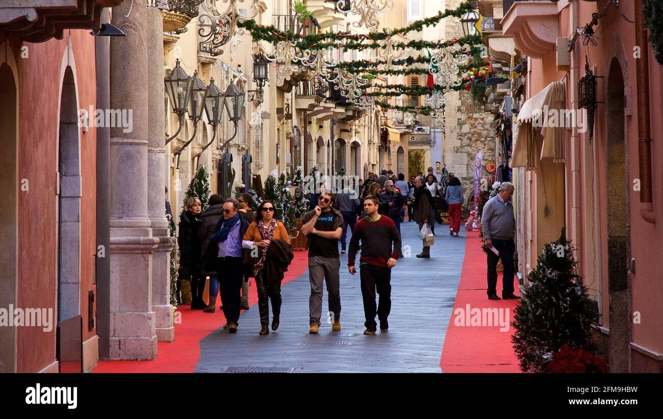 Italia, Sicilia, Taormina, centro città, zona pedonale, Decorazioni natalizie, passanti, edifici storici color salmone a sinistra e a destra Foto Stock