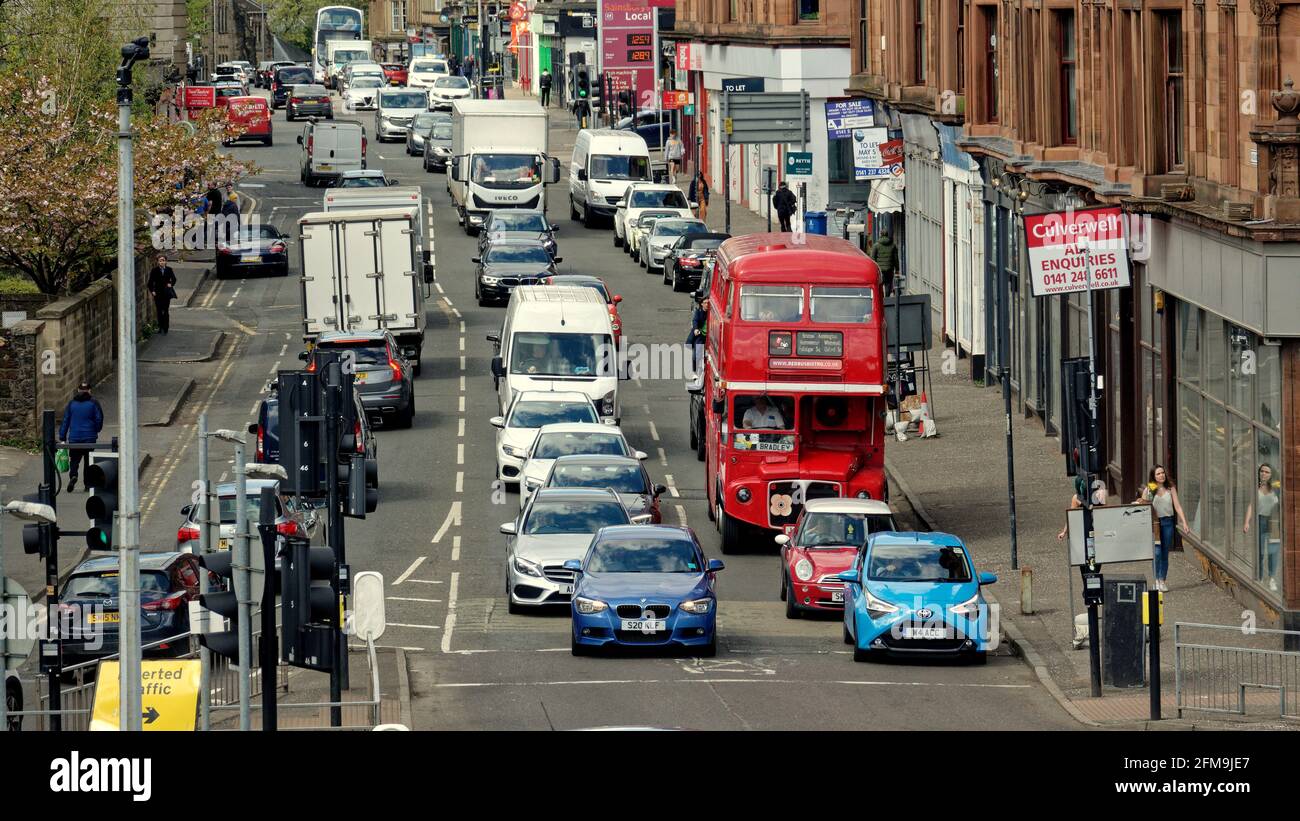 Glasgow, Scozia, Regno Unito. 7 maggio 2021. Regno Unito Meteo: Soleggiato allentamento di blocco ha visto un sacco di footfall con poco da fare, come le persone vagavano da sole e si sedevano molto. Il bus ristorante rosso continua il suo aspetto incongruente come l'ex-padrone di Londra ora un ristorante Red Bus Bistro è bloccato al semaforo su strada boschi nella sua panoramica tour della città con tè pomeridiano. Credit: Gerard Ferry/Alamy Live News Foto Stock