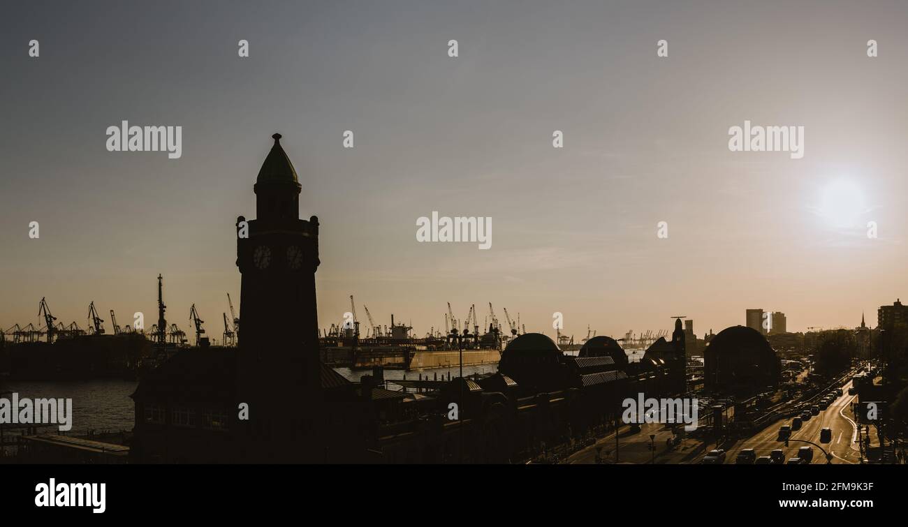 Silhouette di famosi hamburger Landungsbruecken con porto commerciale e il fiume Elba con sole serale, St. Pauli district, Amburgo, Germania Foto Stock
