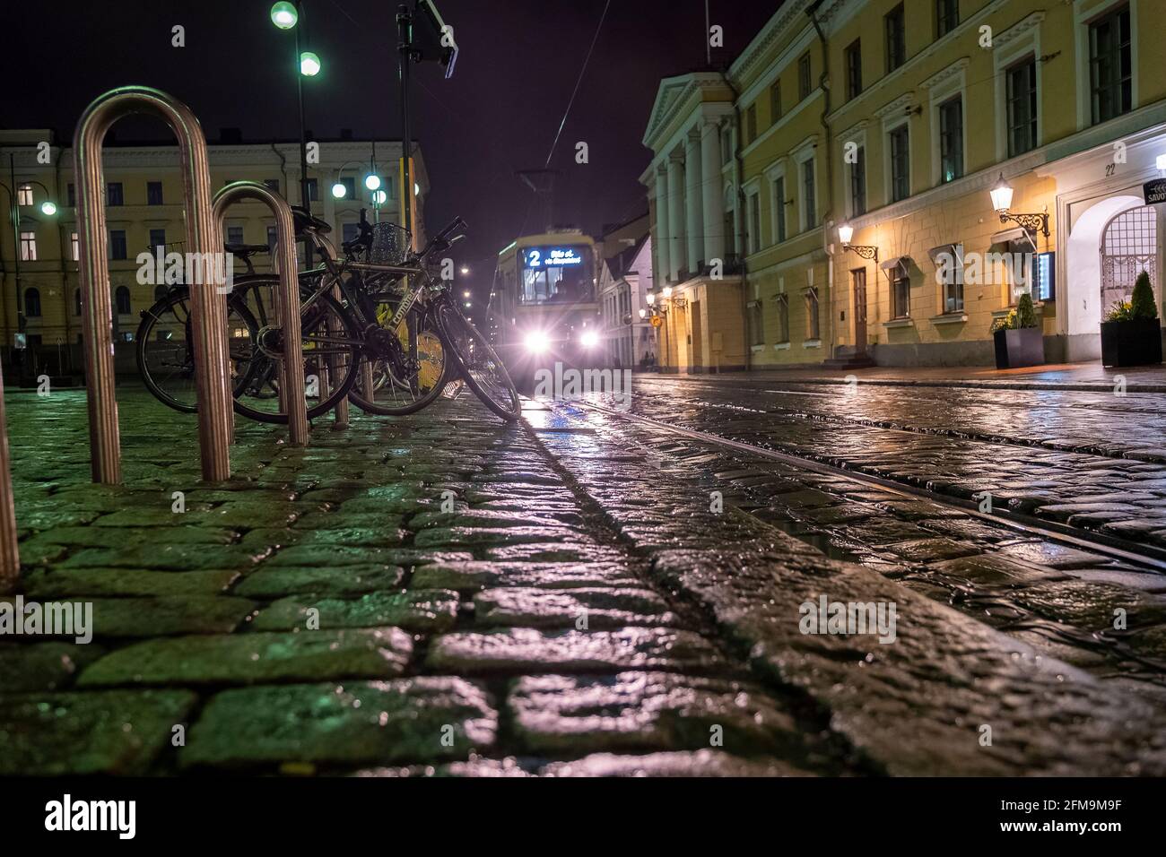 Helsinki / Finlandia - 5 MAGGIO 2021: Un tram che guida su un marciapiede in pietra bagnata nel centro di Helsinki. Foto Stock