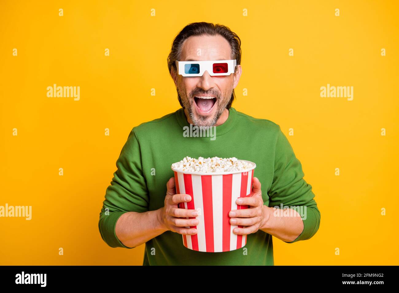 Foto di pazzo ragazzo con setole tenere scatola di carta popcorn usura occhiali 3d verde pullover isolato giallo sfondo Foto Stock