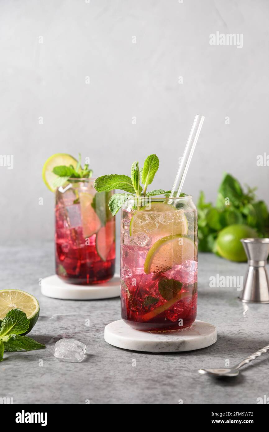 Due mojito di mirtilli con lime, menta e cubetto di ghiaccio su sfondo grigio. Formato verticale. Foto Stock