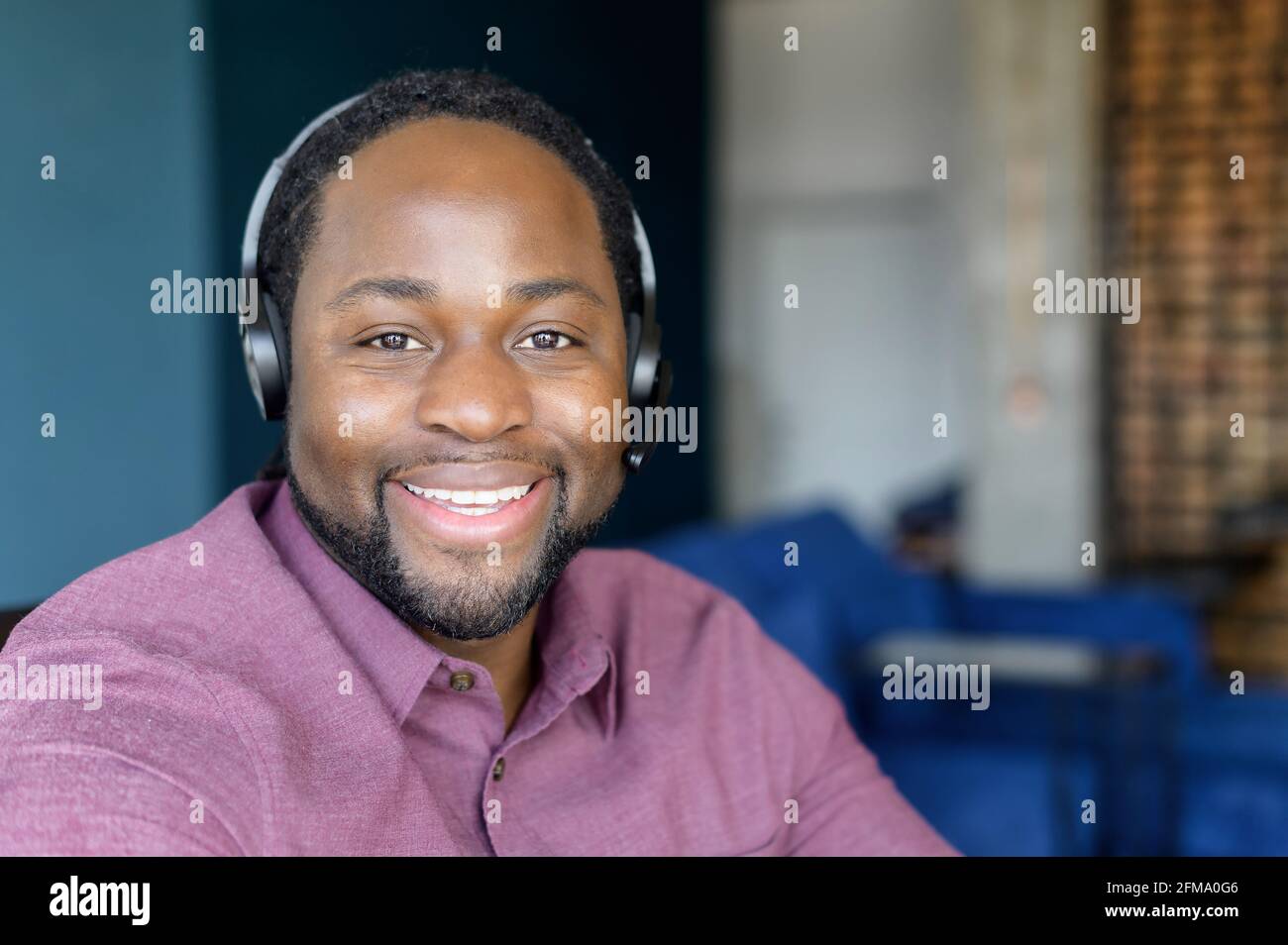 L'operatore del call center indossa le cuffie guarda la fotocamera con un sorriso allegro, un'immagine di un allegro uomo afro-americano in cuffia, un addetto all'assistenza tecnica in cuffia in contatto Foto Stock
