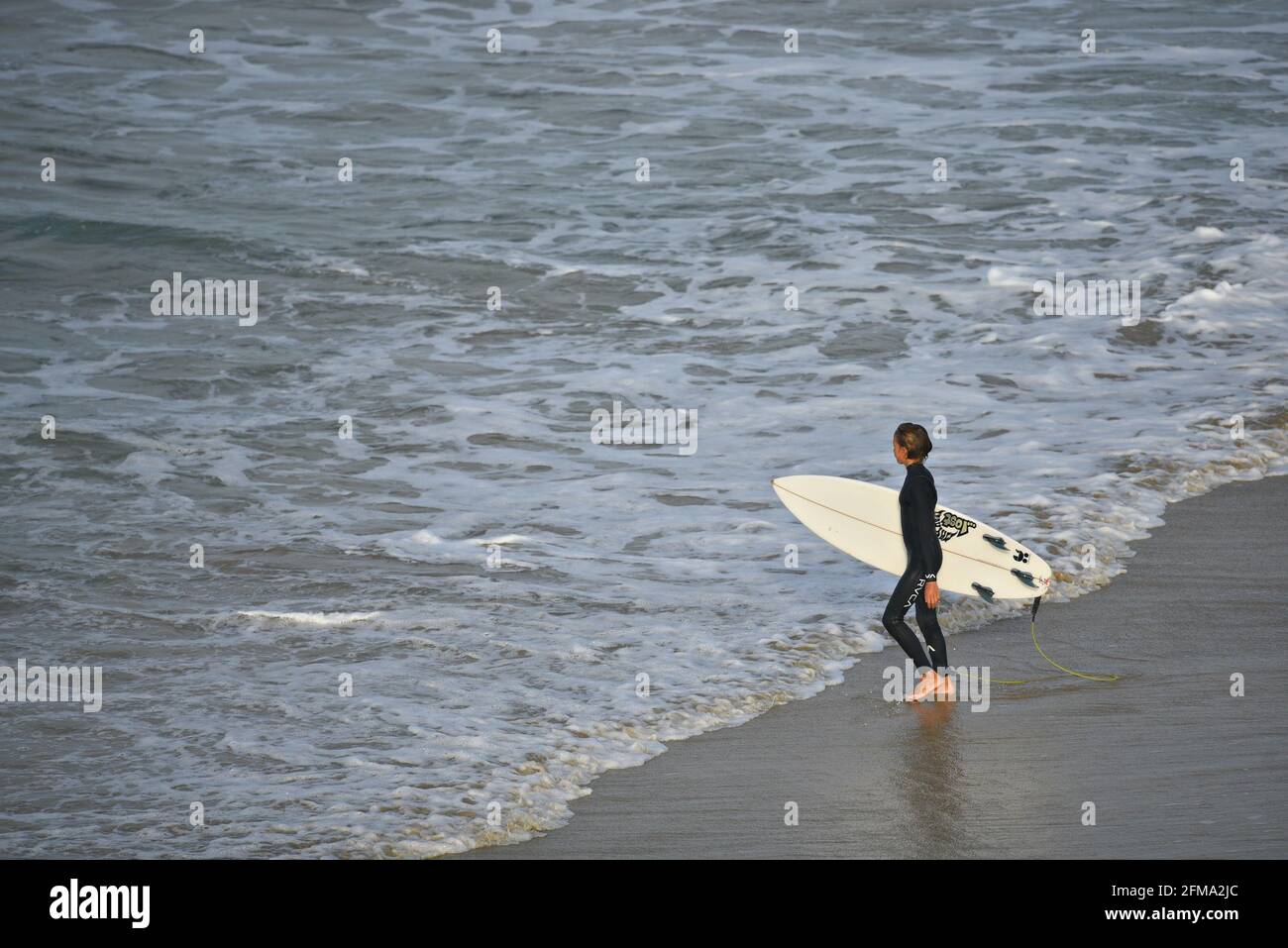 Surfista maschile con la sua tavola da surf sulla costa di Huntington Beach in California, Stati Uniti. Foto Stock