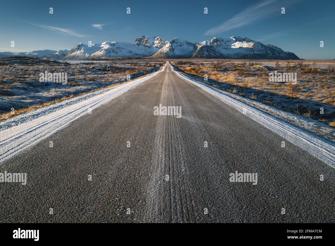 La strada apparentemente infinita conduce attraverso un paesaggio invernale leggermente innevato alla catena montuosa Foto Stock