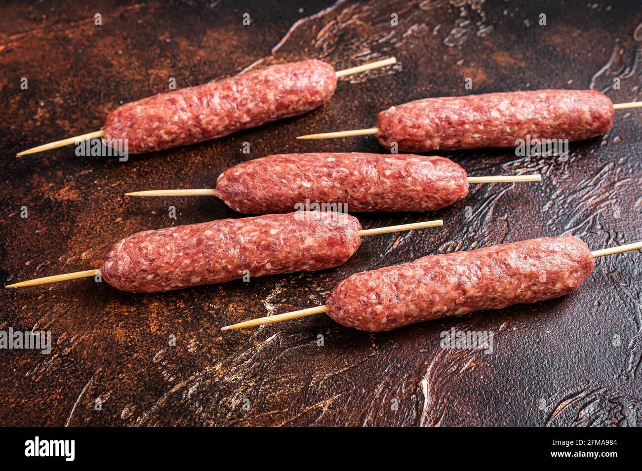 Kebab crudo di carne kofta salsicce su spiedini. Sfondo scuro. Vista dall'alto Foto Stock