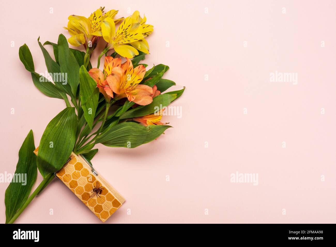 Bouquet estivo con Alstroemeria in giallo e arancio tenuto da una grande clip in legno stampata con un'ape e un nido d'ape pattern su un pallido rosa peloso b Foto Stock