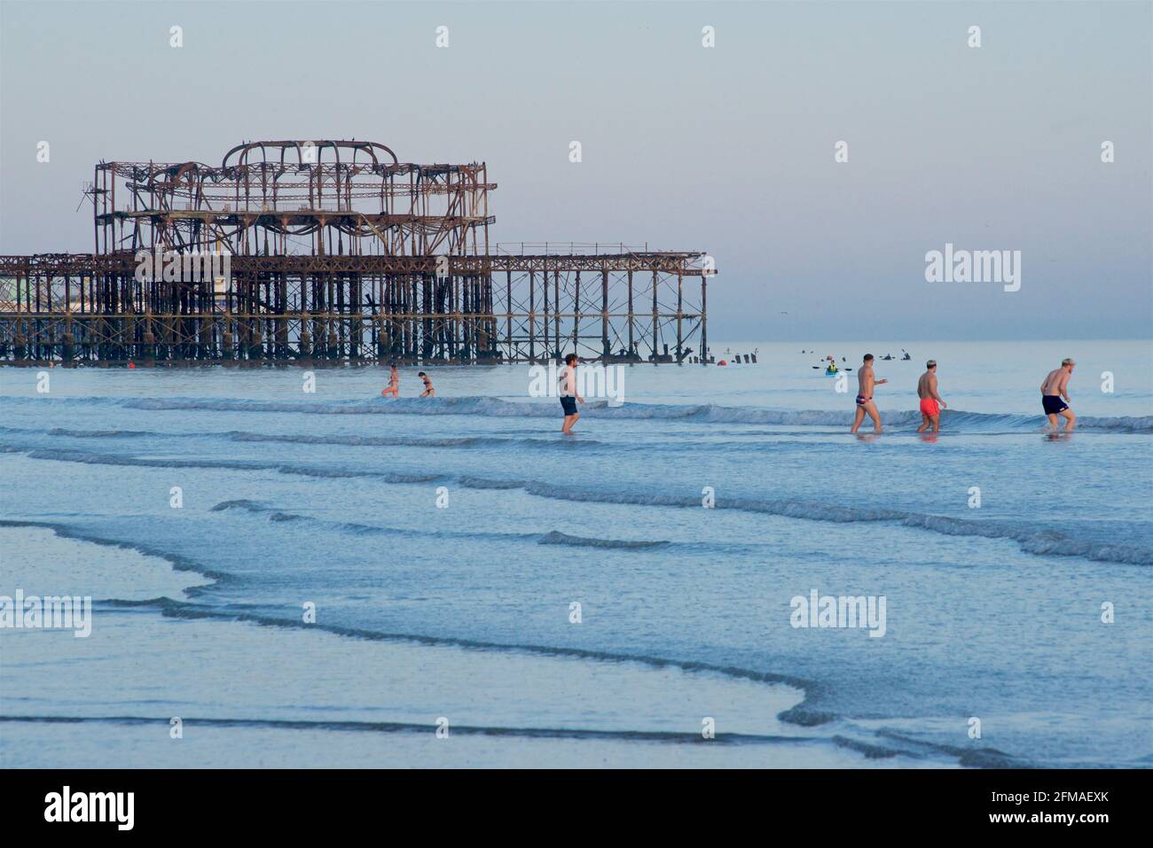 Nuotatori che si dirigono verso l'esterno per un tuffo nella Manica con la bassa marea, i resti arrugginiti del West Pier sullo sfondo. Brighton & Hove, Sussex, Inghilterra, Regno Unito Foto Stock