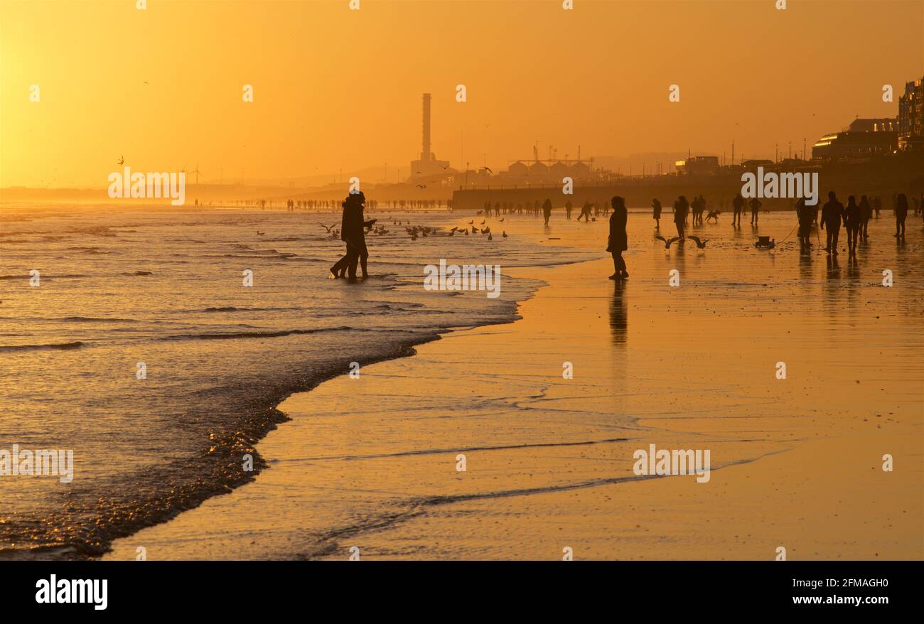 Spiaggia di Brighton e Hove con bassa marea che guarda ad ovest. Sagome di persone che camminano lungo la spiaggia sabbiosa al tramonto. East Sussex, Inghilterra Foto Stock