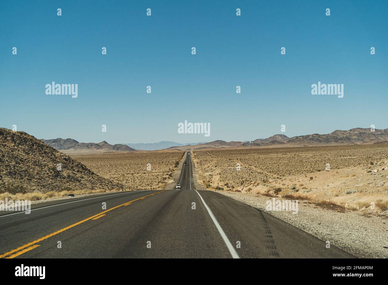 Strada autostradale nel deserto che conduce all'orizzonte contro il blu chiaro cielo e montagne Foto Stock