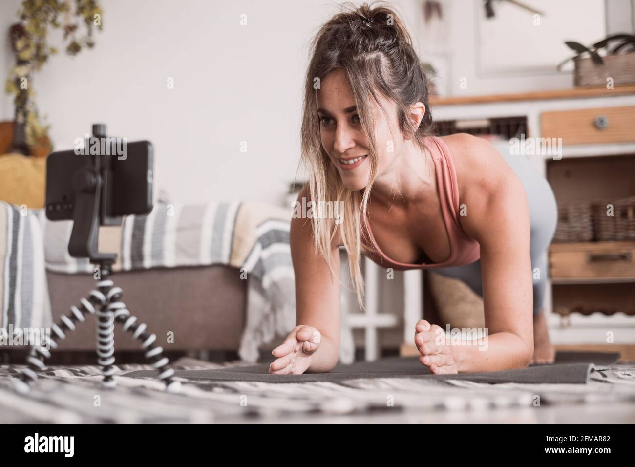 Giovane donna sportiva che lavora a casa, adolescente facendo esercizi di fitness sul pavimento del soggiorno per le natiche corpo che si modellano utilizzando il programma di allenamento personale online con il telefono, facendo yoga pilates al chiuso Foto Stock