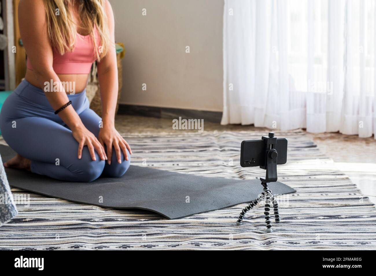 Shot di donna fitness seduta sul tappetino yoga e utilizzando il telefono cellulare. Adatta giovane donna utilizzando il cellulare mentre facendo esercizio a casa. Creatore di contenuti moderni uomini d'affari online internet Foto Stock