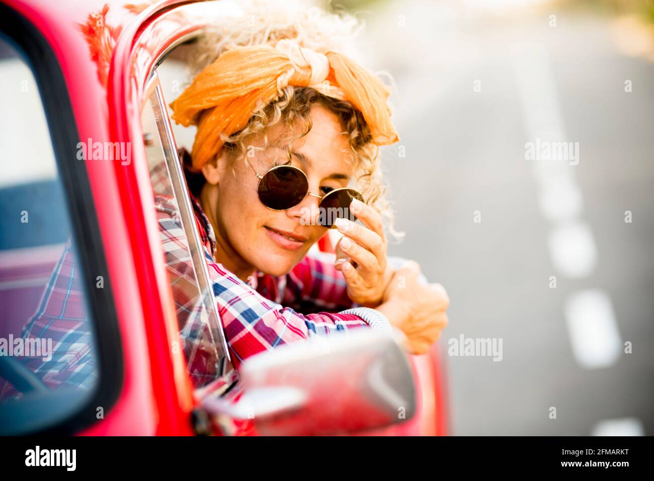 Felice giovane donna adulta sorridere allegro e godere di sedersi all'interno la sua auto trendy rossa pronta per partire e partire per un viaggio o una vacanza - gioiosa donna stile di vita persone indipendenti Foto Stock