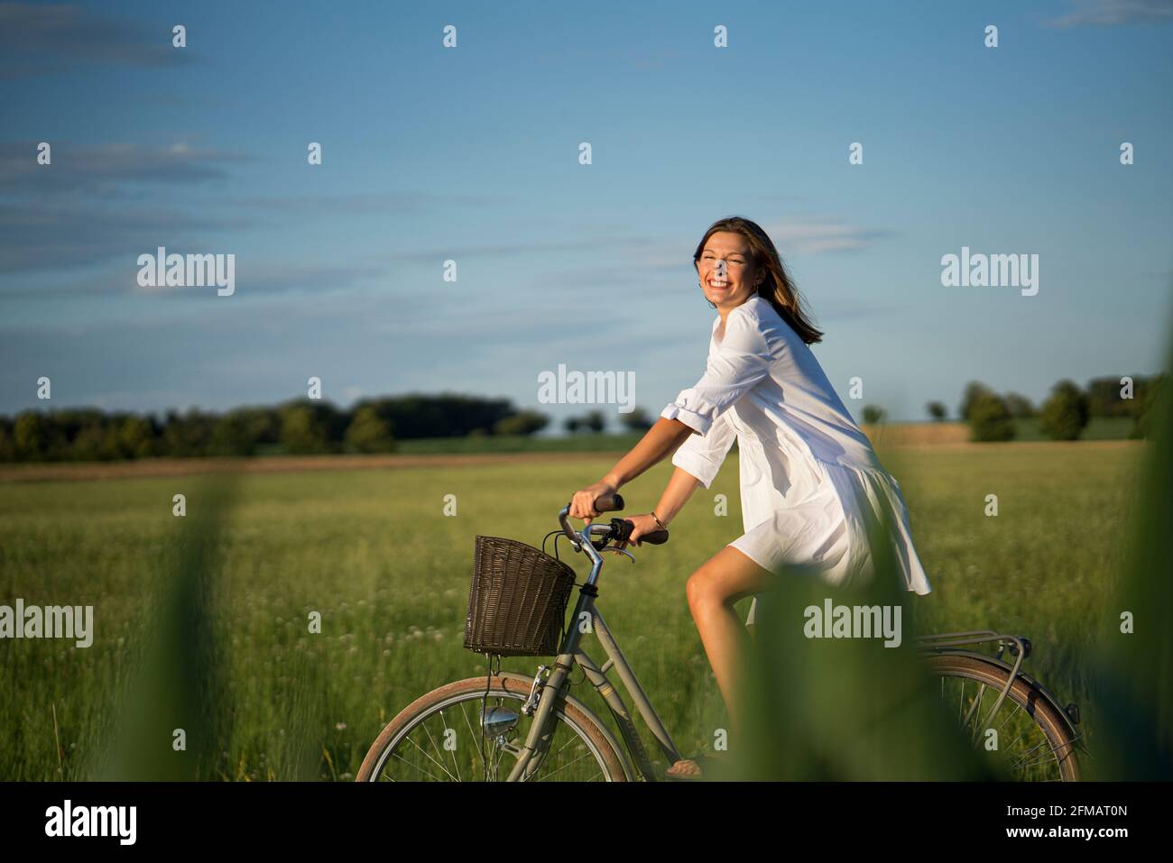 La giovane donna guida una bicicletta con un cesto nell'umore serale, Franconia, Baviera, Germania Foto Stock