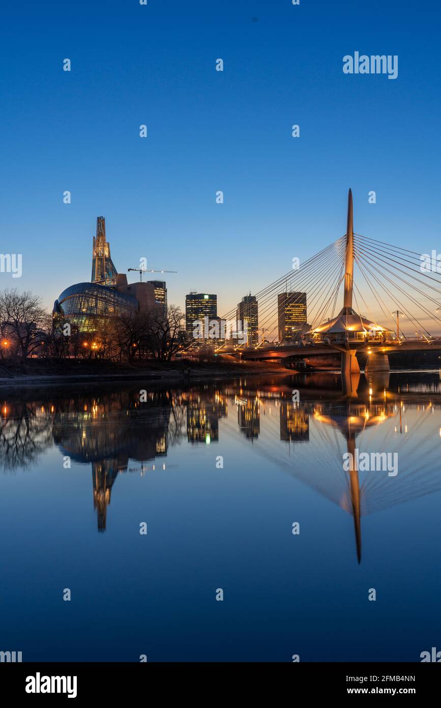 La linea di sklyline della città illuminata al tramonto si riflette nel fiume Rosso, Winnipeg, Manitoba, Canada. Foto Stock