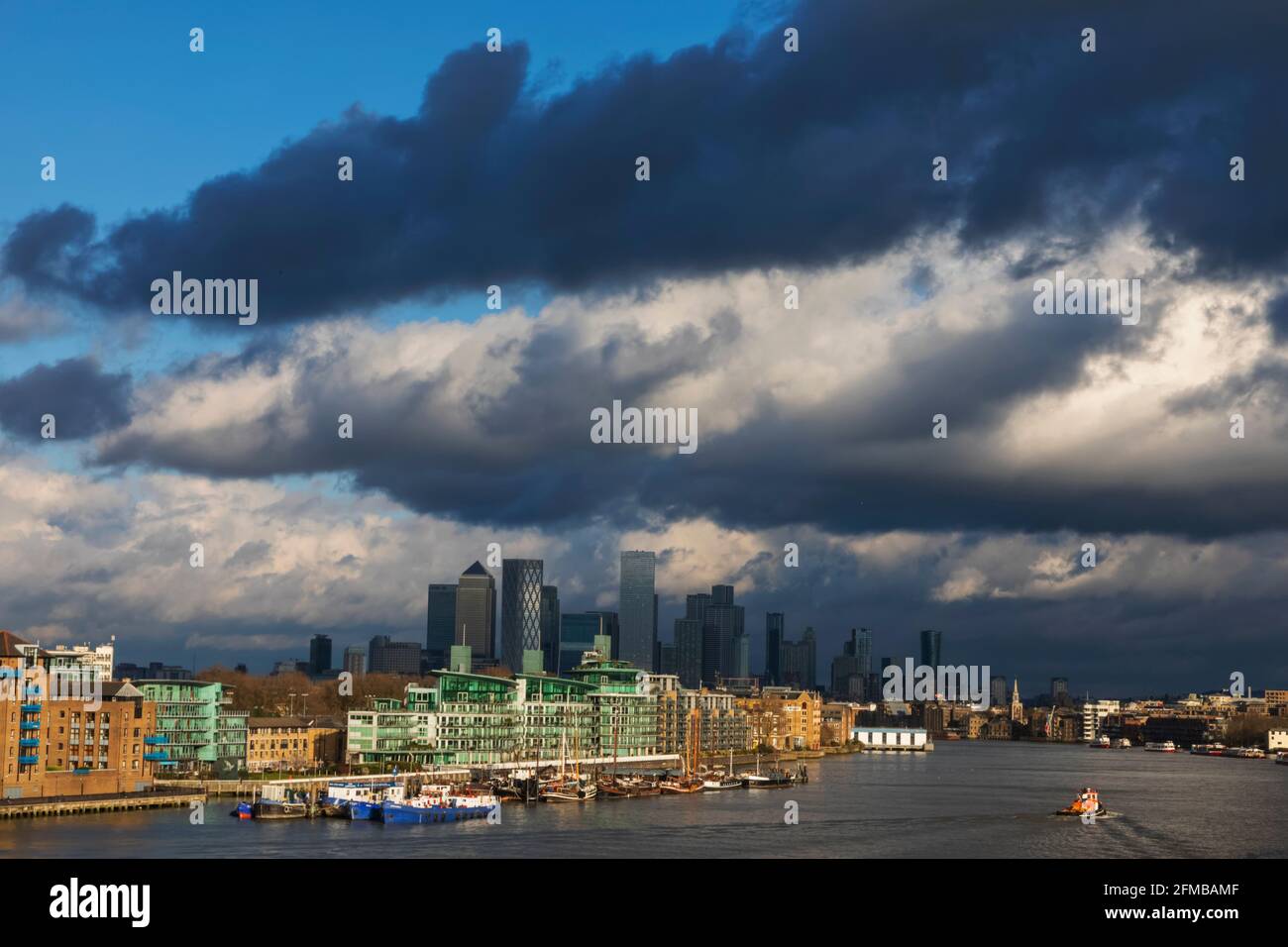 Inghilterra, Londra, Docklands, Fiume Tamigi e Canary Wharf Skyline con luce del tardo pomeriggio sulle spettacolari Nuvole delle tempeste Foto Stock