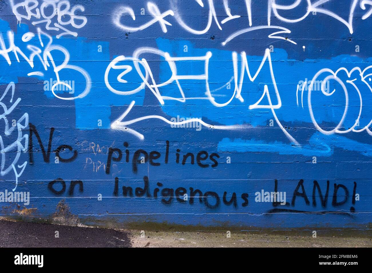 Graffiti urbani e parole che protestano per la costruzione di condotte su terra indigena dipinta su un muro, Vancouver, British Columbia, Canada Foto Stock
