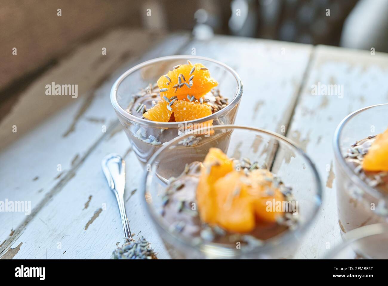 Cucina ayurvedica - mousse al cioccolato con tofu di seta, decorata con filetti di arancio e fiori di lavanda, piccole ciotole di vetro riempite su un tavolo di legno bianco Foto Stock