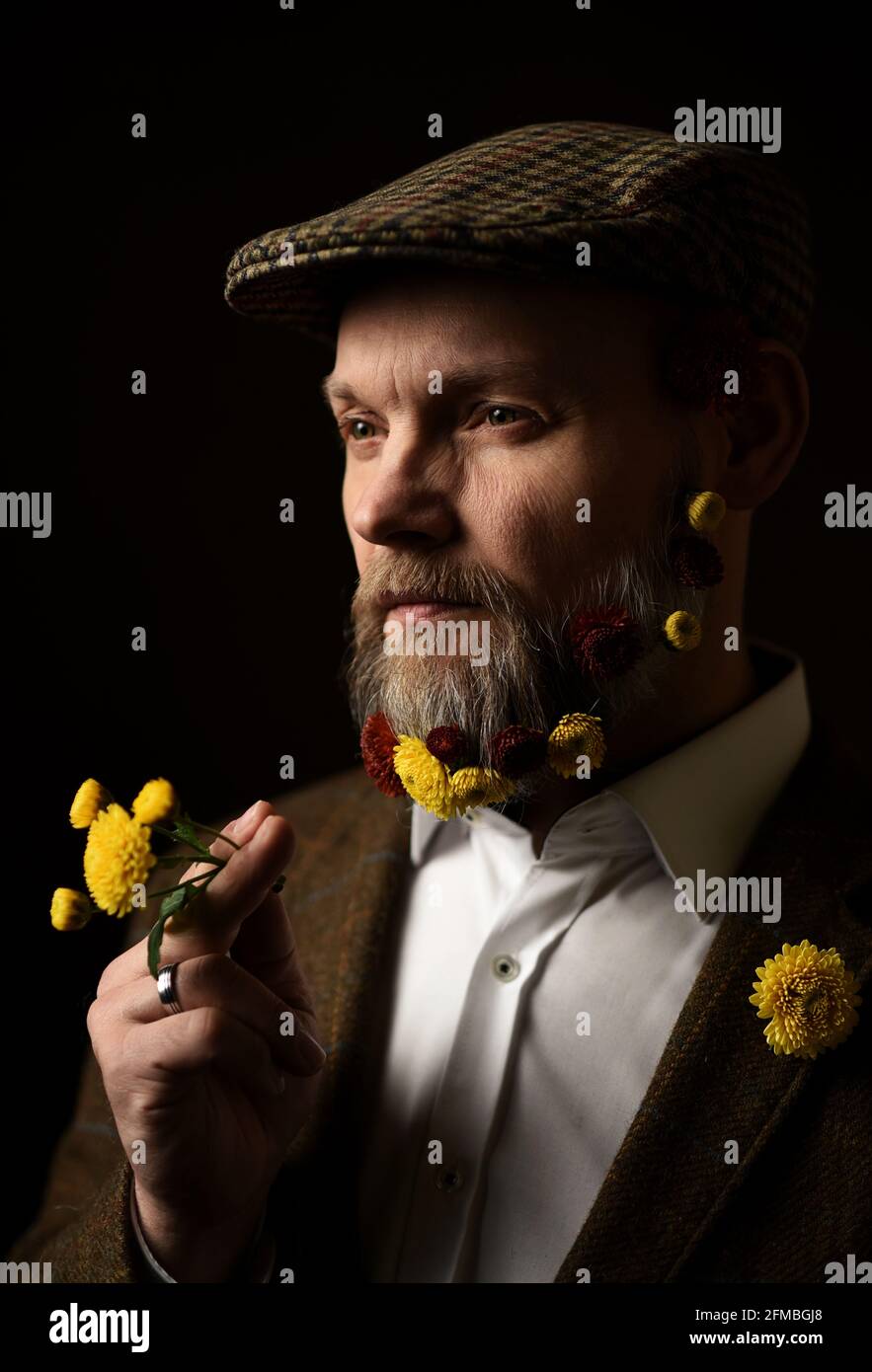 Uomo in una cuffia piatta con fiori nella barba Foto Stock