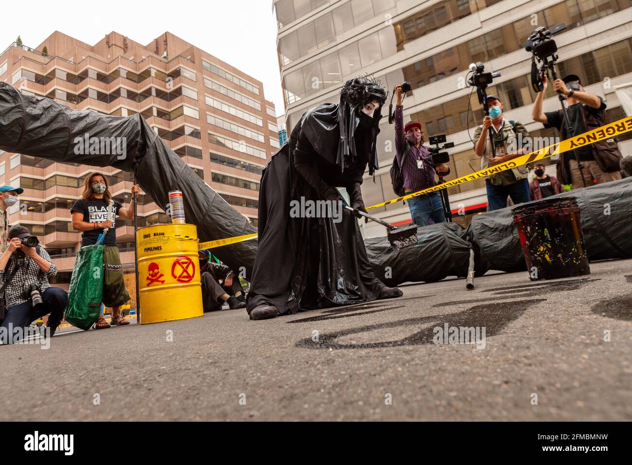 Washington, DC, USA, 7 maggio 2021. Nella foto: Il membro nero della Brigata rossa di Extinction Rebellion usa il petrolio per scrivere la "Stop Line 3" per strada durante una protesta contro Wells Fargo che chiede di smettere di finanziare la costruzione del gasdotto. La linea 3 porterà olio proveniente dalle sabbie bituminose del Canada. Credit: Alison C Bailey / Alamy Live News Foto Stock