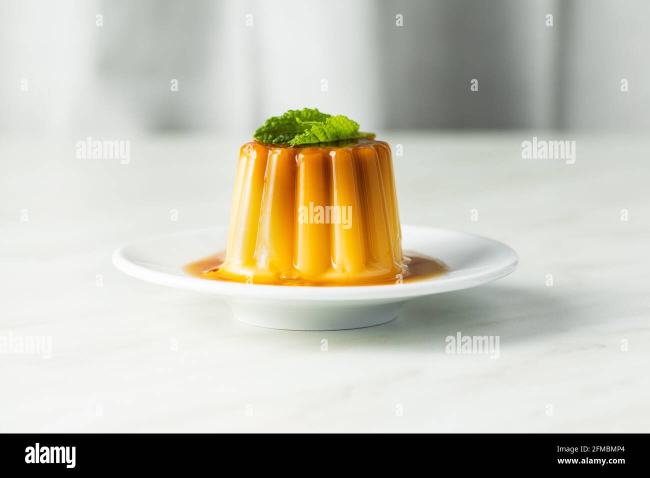 Dolce budino alla vaniglia. Dolce con condimento al caramello su tavola bianca. Foto Stock