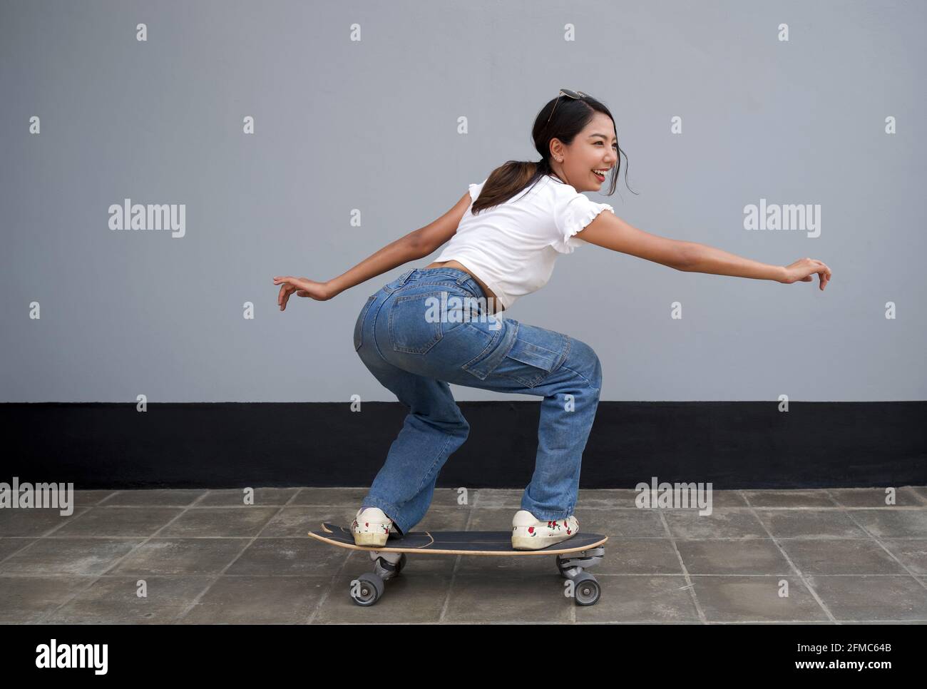 Giovane donna asiatica con occhiali da sole sulla sua testa surf skateboard sulla corsia pedonale. Foto Stock