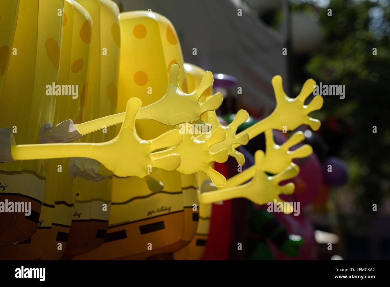 Una lunga linea festiva di grandi, giallo Sponge Bob giocattoli gonfiabili con armi e mani estese in un'onda, visto dalla parte posteriore, per la vendita ad un festival. Foto Stock
