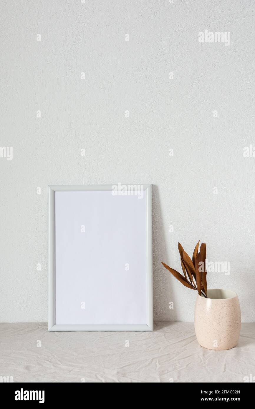 Casa decoratore moccap, quadro vuoto cornice vicino bianco dipinto muro di cemento, rami con foglie asciutte Foto Stock