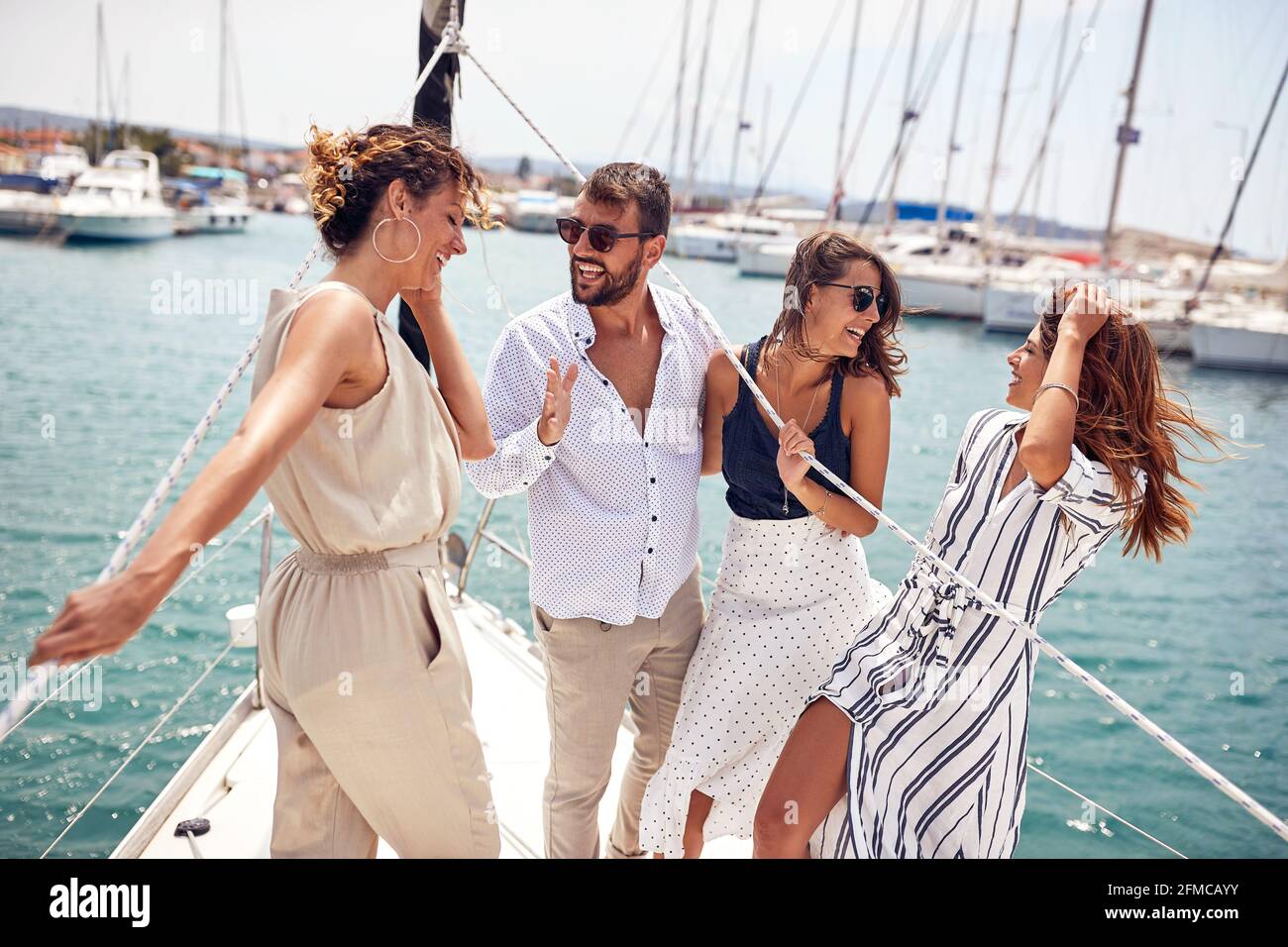 Un gruppo di modelli giovani e belli è in piedi sul prua dello yacht e avere un bel tempo cavalcando attraverso il molo in una bella giornata estiva Foto Stock