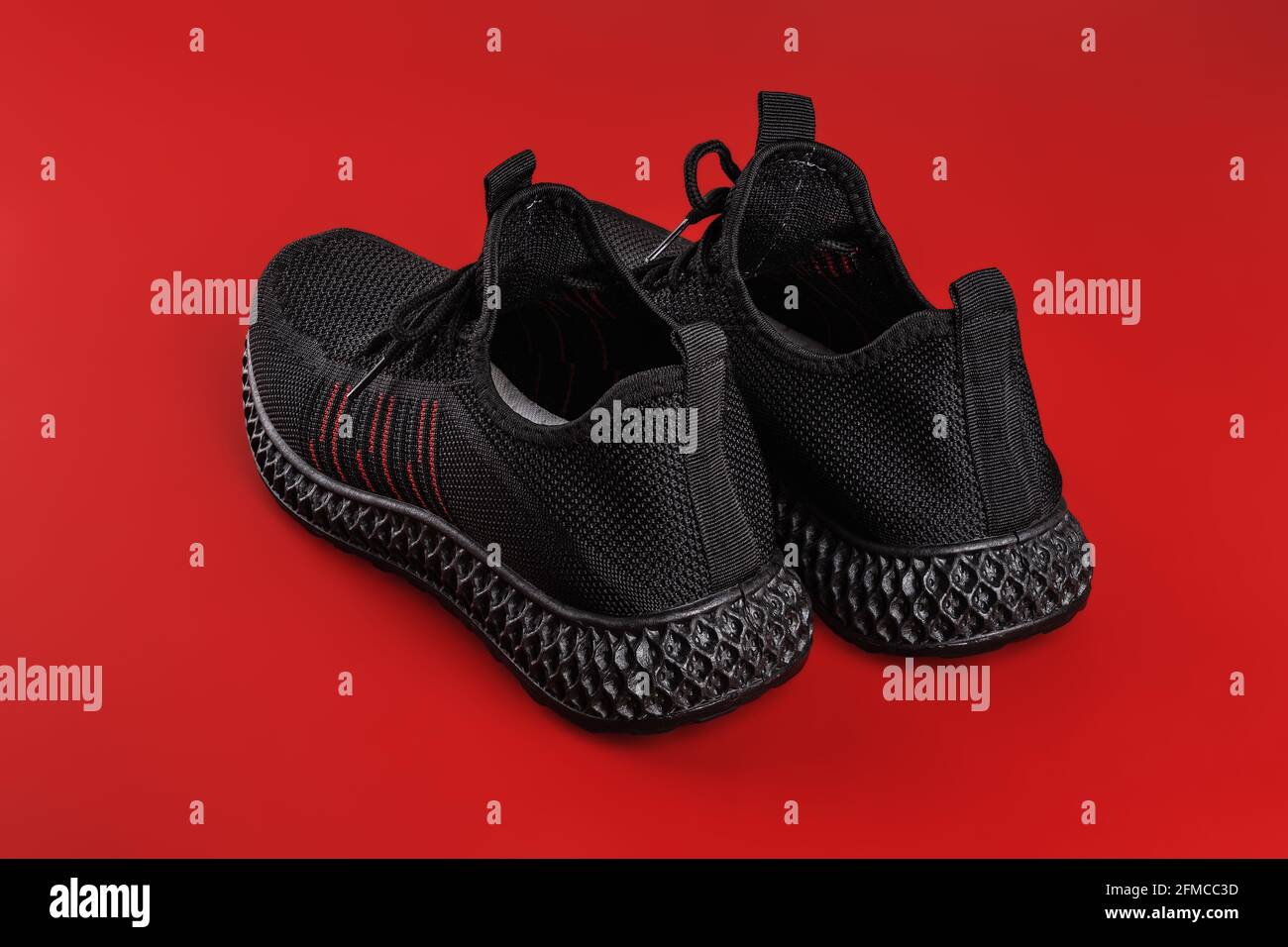 Vista posteriore delle sneaker in mesh nera su sfondo rosso. Paio di scarpe moderne traspiranti per un'estate calda. Nuove comode scarpe da uomo per uno stile di vita attivo. Foto Stock