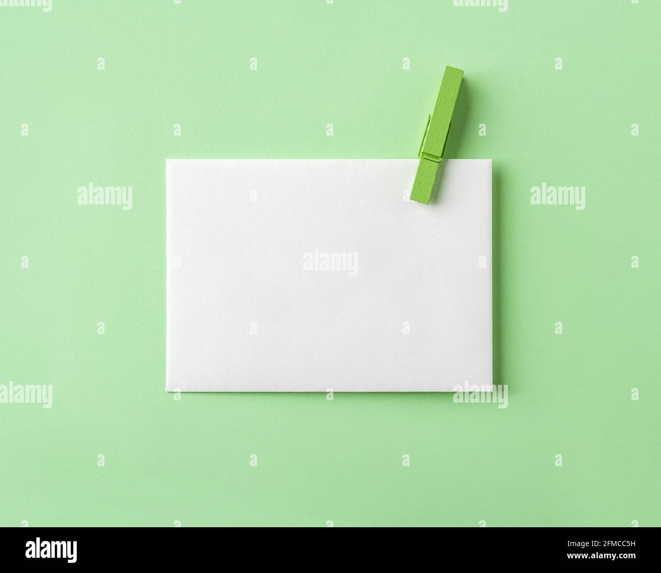 Carta bianca bianca con spilla di legno verde su sfondo di carta verde pastello. Modello dal design minimalista per un messaggio e un biglietto d'auguri ecologici Foto Stock