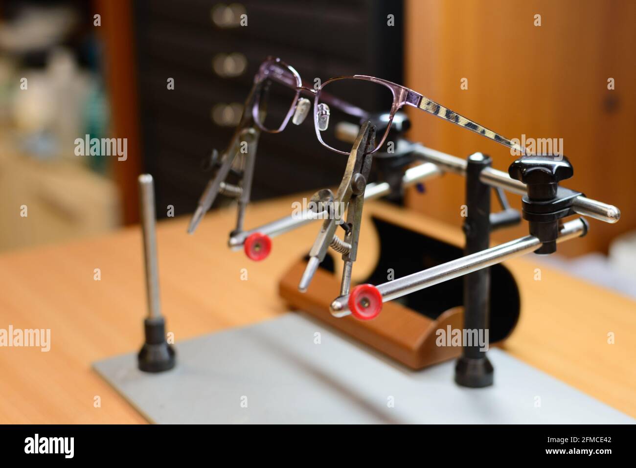 Primo piano della foto degli occhiali da lettura pronti per la riparazione mentre vengono fissati al supporto del saldatore manuale. Foto Stock