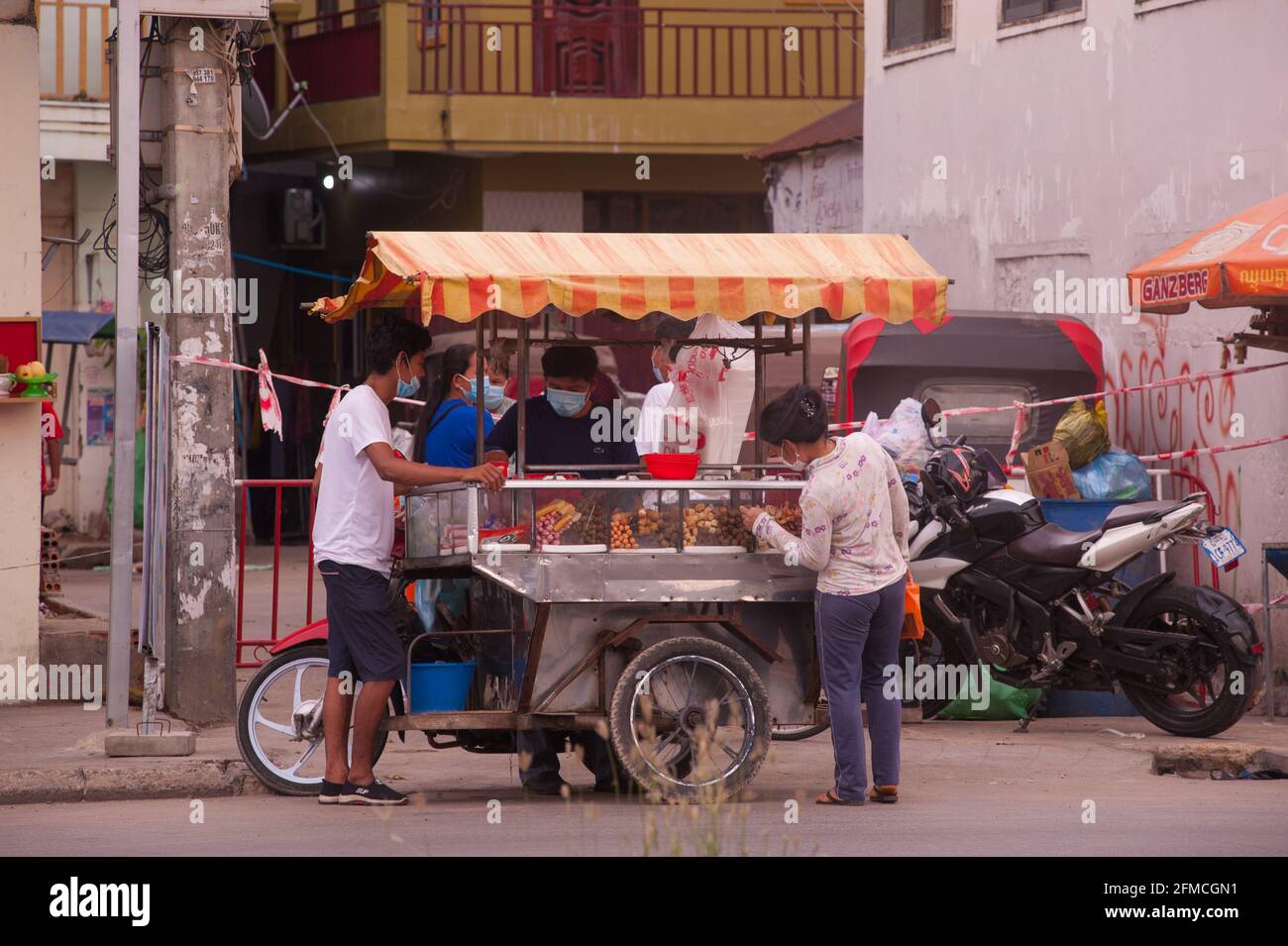Phnom Penh, Cambogia. 8 maggio 2021. Dopo 3 settimane di chiusura totale della città, il governo ha diviso Phnom Penh in 3 zone colorate (rosso, arancione e giallo) a causa dell'aumento di COVID in corso. Qui, un carrello mobile di cibo sta vendendo barbecue all'ingresso di una 'zona arancione', Credito: Kraig Lieb / Alamy Live News Foto Stock